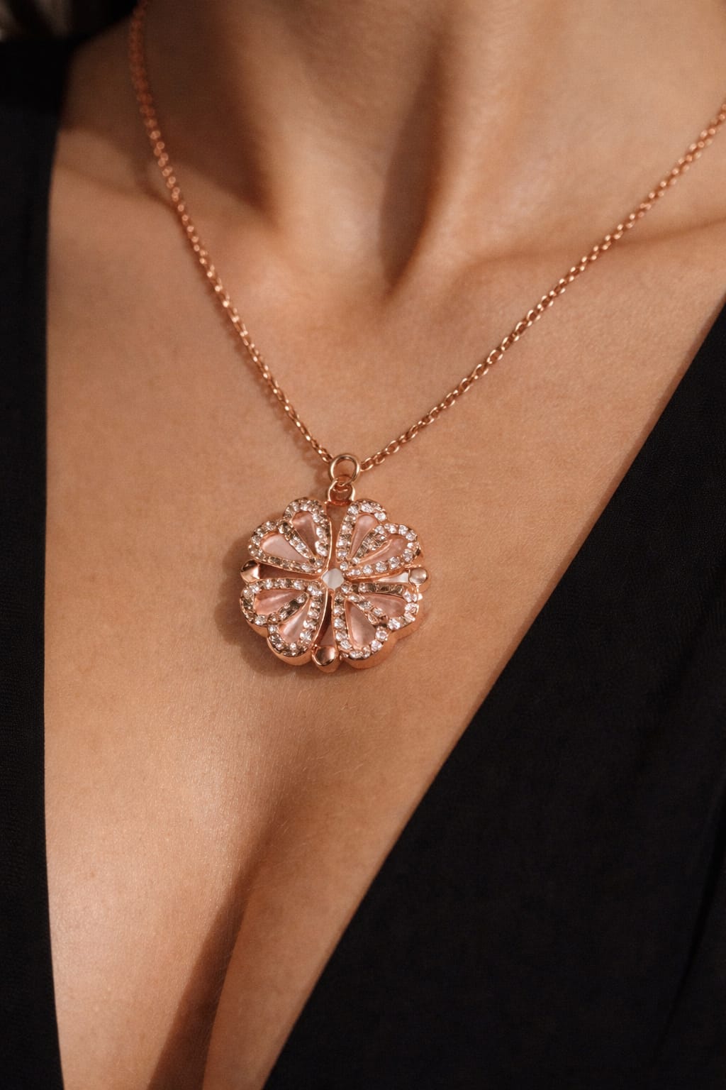 Rose gold necklace with a detailed pendant on a person wearing a black top.